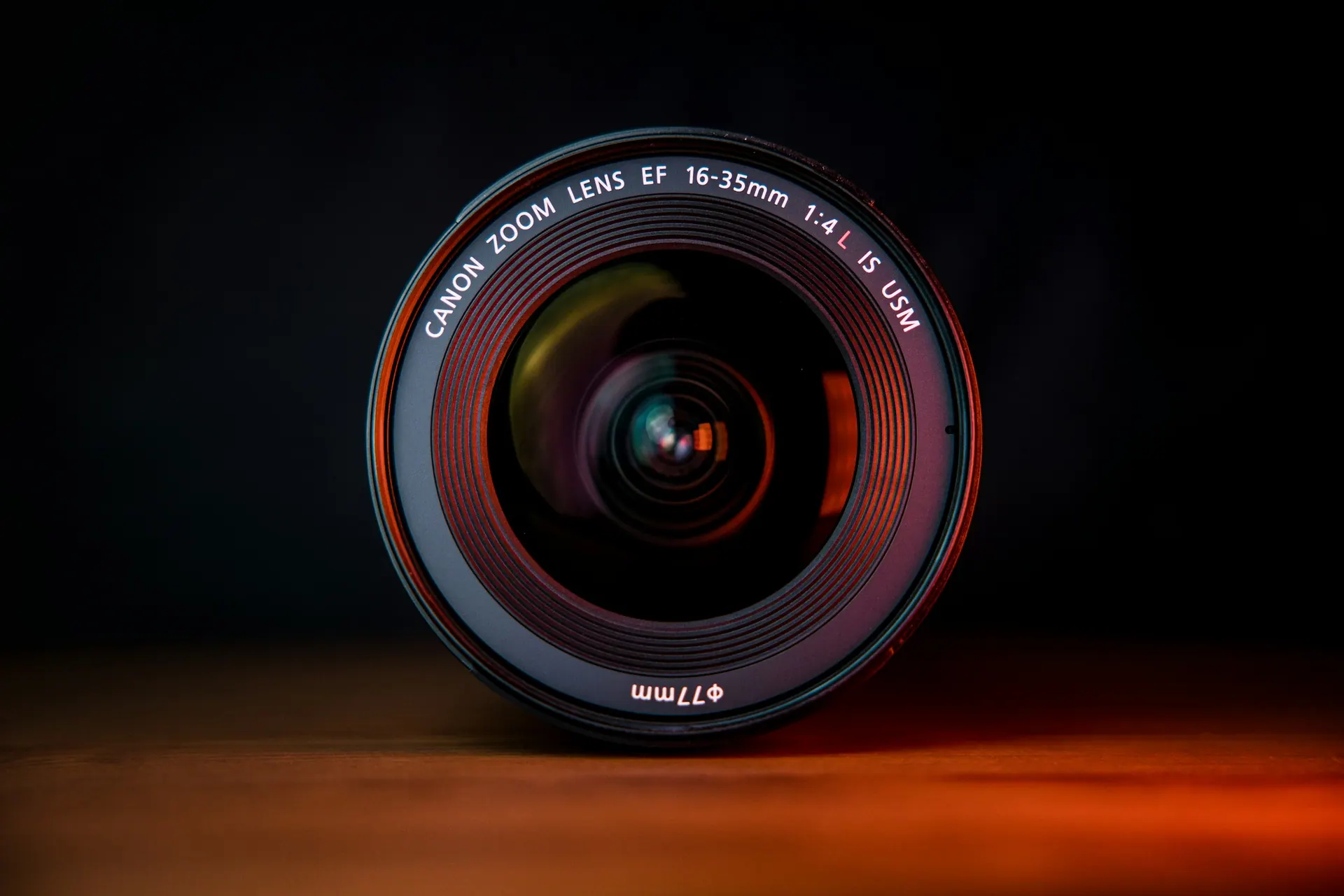 A camera lens with reflective coatings showing blue and amber highlights across the glass.