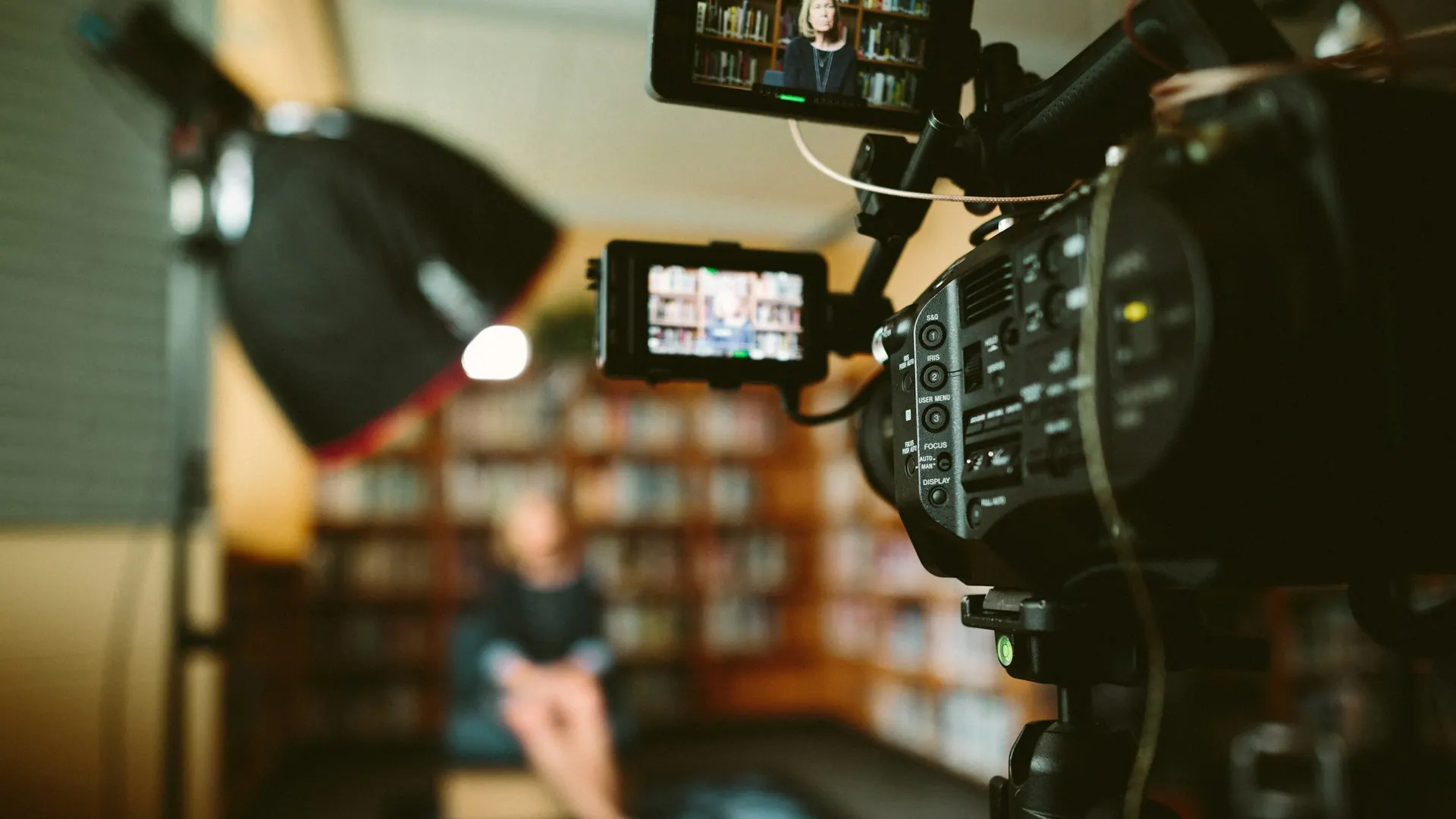 A video camera mounted on a tripod during filming, with a monitor showing the framed shot.