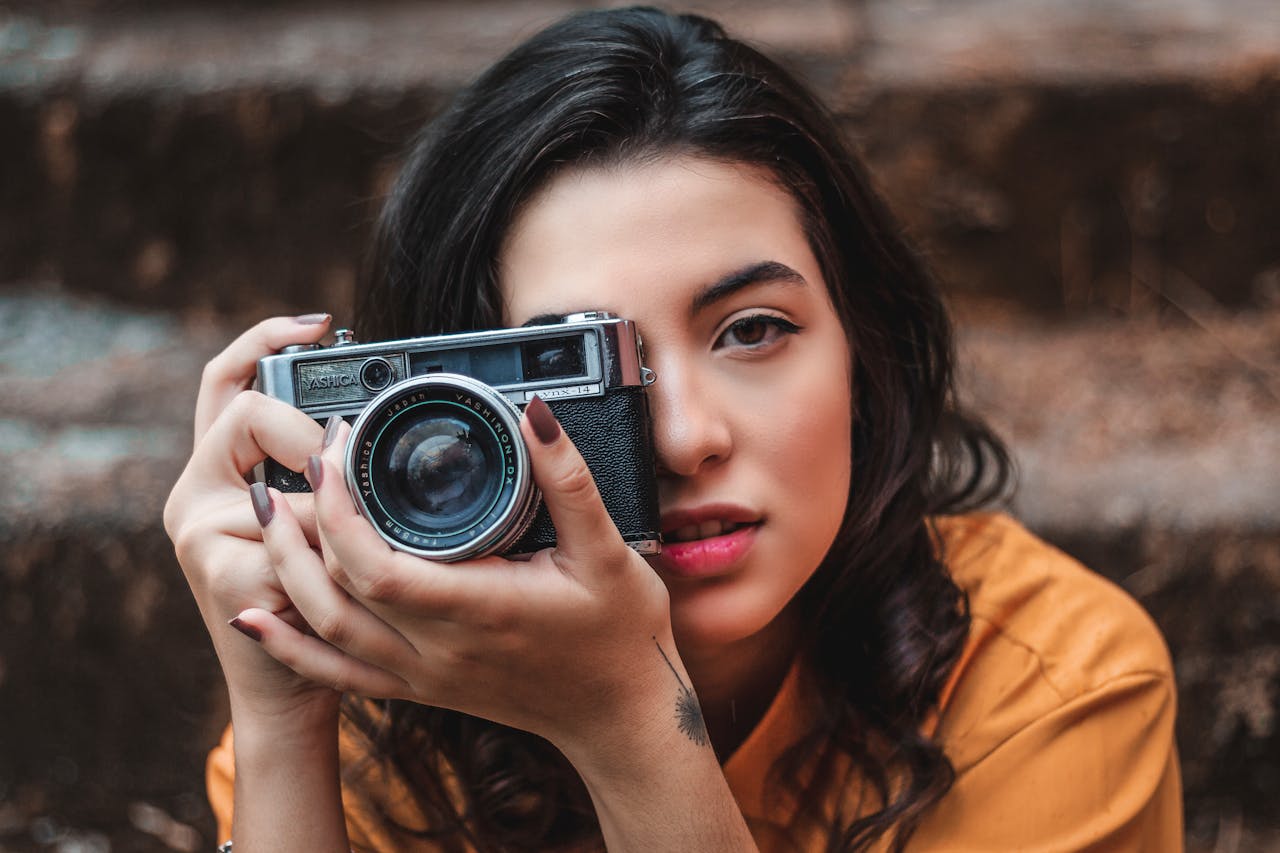 Portrait of a stylish young woman holding a vintage camera outdoors.
